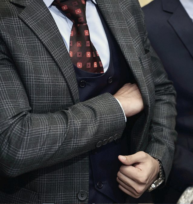 Man buttoning a grey check blazer over a navy waistcoat