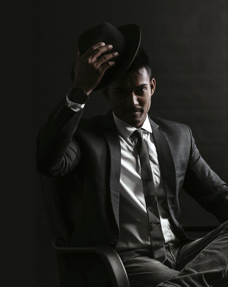 Man in a tailored grey check suit tipping a black fedora