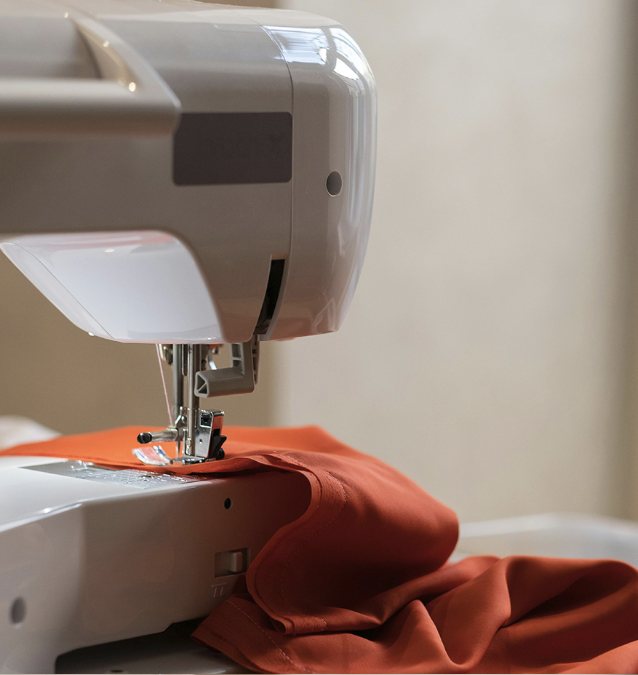 Sewing machine stitching a rust-orange garment in the Aayra studio