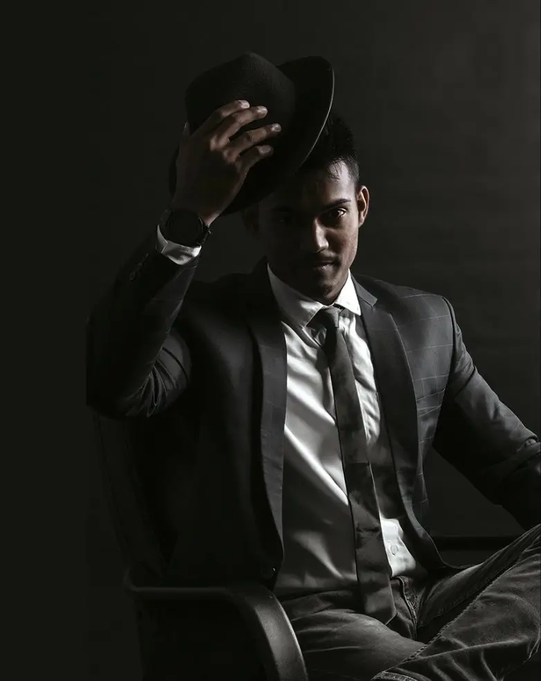 Man in a tailored grey check suit tipping a black fedora
