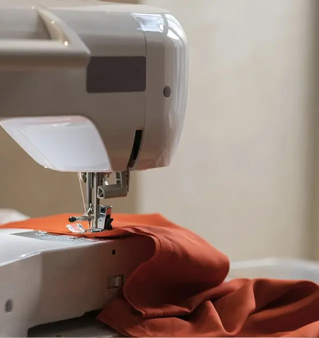 Sewing machine stitching a rust-orange garment in the Aayra studio