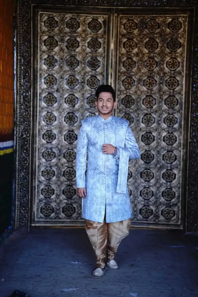 Man in a powder-blue Aayra sherwani in front of a carved door